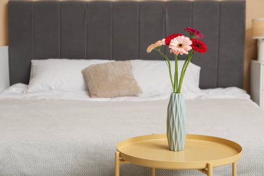 Yatak odasındaki masada Gerbera çiçekli vazo.