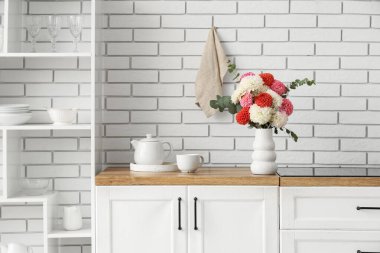 Çok güzel çiçekleri olan vazo ve ahşap mutfak tezgahında hafif tuğla duvarın yanında çay.