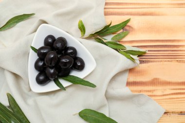 Lezzetli siyah zeytinli tabak ve ahşap arka planda yapraklar.