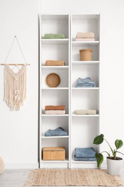 Odadaki ışık duvarının yanında giysi, dekor ve saksı bulunan raf ünitesi.