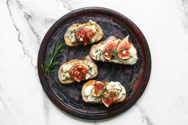 Beyaz zemin üzerinde ricotta ve mavi peynirli lezzetli incirli bruschetta tabağı.