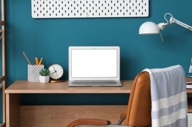 Boş dizüstü bilgisayarı, masa lambası ve mavi duvarın yanında tahta tahtası olan şık bir iş yeri. Serbest konsept