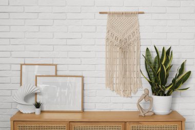 Beyaz tuğla duvarın yanındaki çekmecelerde fotoğraf çerçeveleri, biblo ve ev bitkisi.