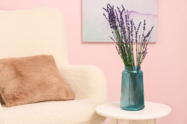 Oturma odasındaki koltuğun yanındaki masada lavanta çiçekli vazo.