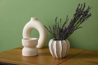 Yeşil duvarın yanındaki masada lavanta çiçekli vazo ve dekor var.