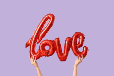 Leylak arka planında aşk kelimesi şeklinde balonu olan kadın eller. Sevgililer Günü kutlaması