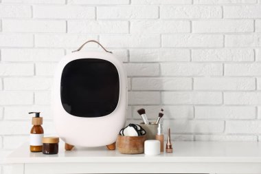 Odadaki beyaz tuğla duvarın yanındaki masada kozmetik ürünleri olan kapalı küçük bir buzdolabı. Yakın çekim.