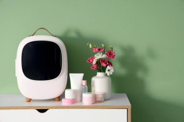 Kozmetik ürünleri ve vazodaki çiçeklerle dolu kapalı küçük bir buzdolabı. Yakın çekim.