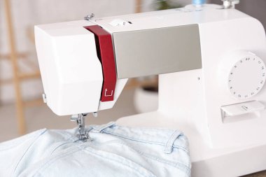Atölyede kot pantolon giyen modern dikiş makinesi, yakın plan.