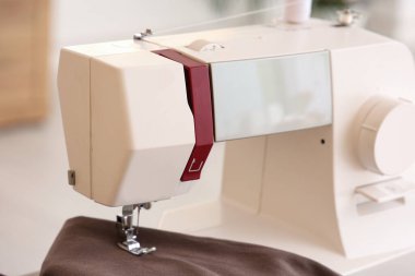 Atölyede kahverengi kumaşlı modern dikiş makinesi, yakın plan.