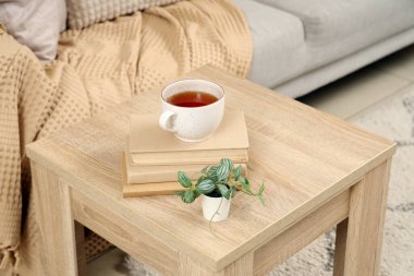 Oturma odasında kitap ve bitki dolu bir fincan çay, yakın plan.