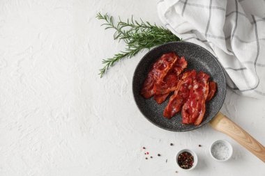 Kızarmış pastırmalı tava, biberiye ve beyaz arka planda bir kase biberli mısır.