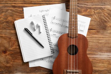 Ukulele, kulaklıklar, defter ve ahşap arka planda notalar