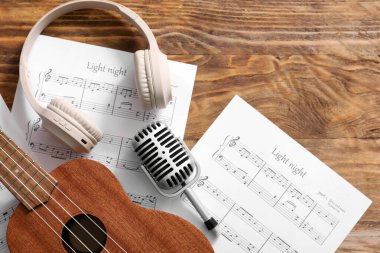 Ukulele, mikrofon, müzik kağıtları ve ahşap arka planda kulaklıklar