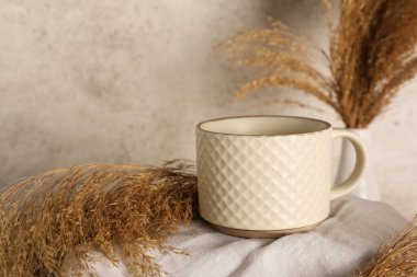 Açık grunge arka plan üzerinde kuru sazlıklar ile beyaz seramik kupa