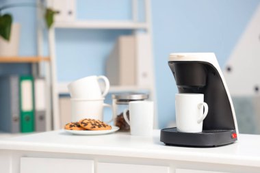 Ofisteki kahve makinesinde fincanlar ve kurabiyeler var.