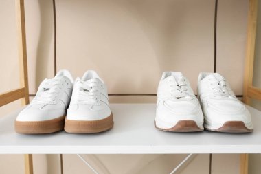 Bej fayans duvarının yanındaki rafta beyaz spor ayakkabılar, yakın plan.