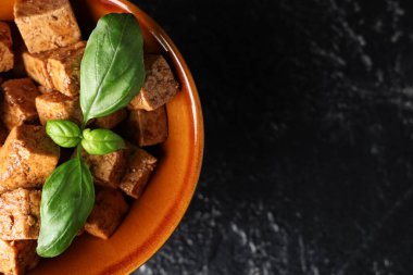 Siyah arka planda kızarmış tofu peyniri ve fesleğenli kase, yakın plan.