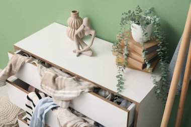 Oturma odasında yeşil duvarın yanında dağınık giysilerle tuvalet, yakın plan.