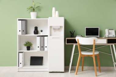 Modern su soğutucusu, çalışma alanı ve raf ünitesi olan şık bir ofis.