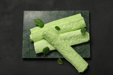 Siyah arka planda rulo yeşil lavaş ve ıspanak olan tahta