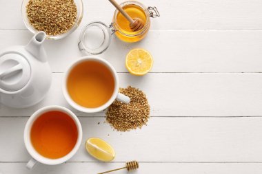 Bardaklar ve çaydanlık dolusu sıcak karabuğday çayı. Beyaz ahşap arka planda limon ve bal kavanozu.