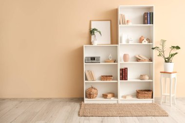 Bej duvarın yanında kitap, dekor ve çiçek rafları