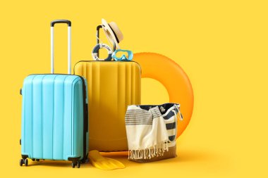 Şişme yüzüklü bavullar, yaz çantası ve sarı arka planda plaj aksesuarları. Tatil kavramı