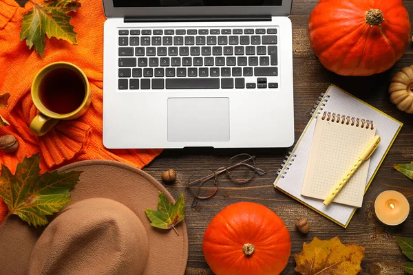 Not defterleri, çay fincanı ve ahşap arka planda sonbahar dekoru olan dizüstü bilgisayar.