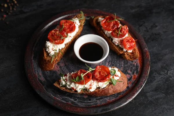 Lezzetli domates bruschetta ile ricotta ve siyah arka planda bir kase sos.