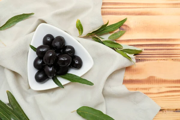 Lezzetli siyah zeytinli tabak ve ahşap arka planda yapraklar.