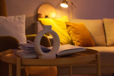 Sehpa, vazo ve kanepenin yanında açık bir kitap. Şık bir oturma odasında, yakın plan.