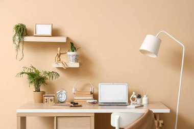 Ofisin içindeki bej duvarın yanında boş dizüstü bilgisayarı olan mucit işyeri.