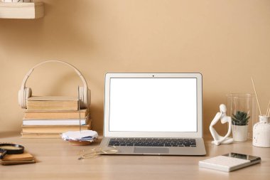 Boş dizüstü bilgisayarı ve ofisteki bej duvarın yanında kitapları olan mucit işyeri.