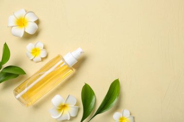 Saç spreyi şişesi, bitki dalları ve renk arka planında tropikal çiçekler olan kompozisyon