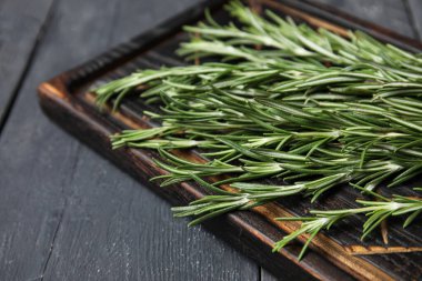 Siyah ahşap arka planda taze biberiye dallarıyla kesme tahtası, yakın plan.