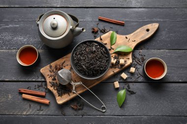 Siyah çay yapraklı kase ve siyah ahşap arka planda çaydanlık.