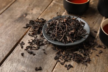 Ahşap arka planda kuru siyah çay yapraklarıyla kaplanmış, yakın plan.