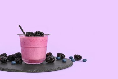 Bir bardak taze böğürtlen suyu ve leylak arkaplanda yaban mersini.