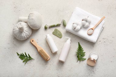 Bitkisel poşetler, yüz masajı aletleri ve bej grunge arka planda bir şişe kozmetik ürünü içeren spa kompozisyonu.