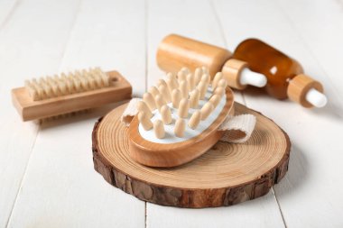 Beyaz ahşap arka planda vücut masajı fırçaları ve kozmetik yağ şişeleri, yakın plan