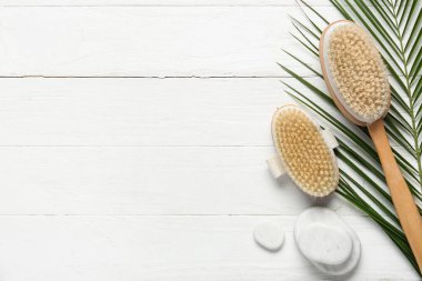 Beyaz ahşap arka planda kaplıca taşlı vücut masajı fırçaları ve palmiye yaprağı