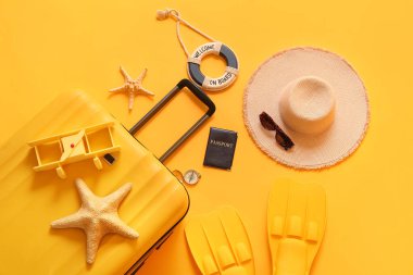 Sarı arka planda bavul, pasaport, palet ve plaj aksesuarları, yakın plan.