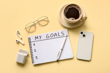 Mesajlı defter. Hedeflerim, cep telefonu ve bej arka planda bir fincan kahve.
