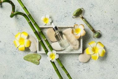 Taşlarla, yüz masajı aletleriyle, tesisat çiçekleriyle ve gri grunge arka planda bir şişe kozmetik ürünüyle güzel bir spa kompozisyonu.