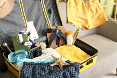 Kanepede erkek mayosu ve plaj aksesuarlarıyla valizi aç, yakın plan.