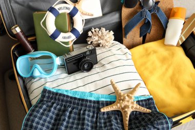 Kanepede erkek mayosu ve plaj aksesuarlarıyla valizi aç, yakın plan.