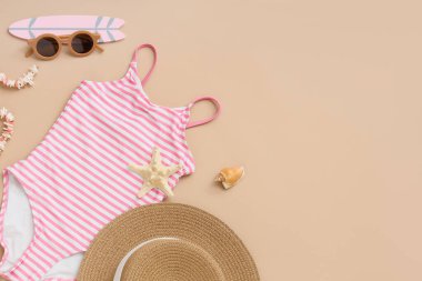 Bej arka planda plaj aksesuarları olan çocuk mayosu.