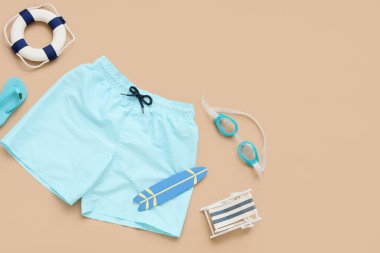 Bej arka planda plaj aksesuarları olan çocuk yüzme şortu.