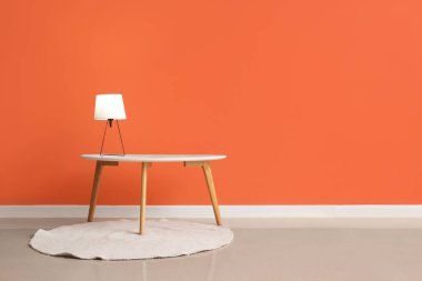 Turuncu duvarın yanında parlayan lamba olan kahve masası.